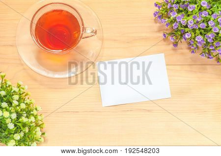 Paper note with teacup and flowers on wood background