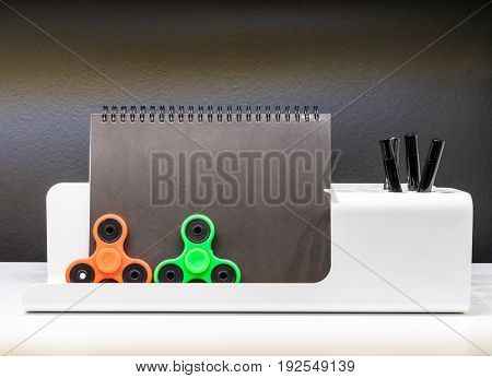 Orange and green fidget spinners with stationary set on white table.
