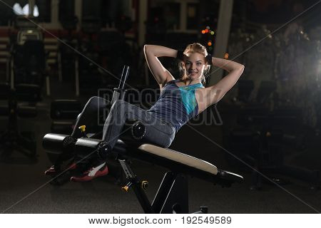 Woman doing strength exercises for abdominal muscles at indoor sport gym. Girl doing yoga stretches after running. Fitness model in dark sport club.