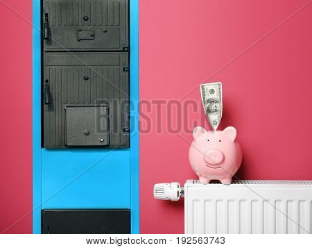 Energy savings concept. Solid fuel boiler, radiator with piggy bank and money on color background