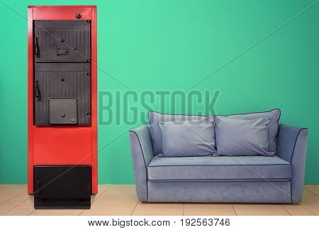 Energy savings concept. Solid fuel boiler and couch on color wall background