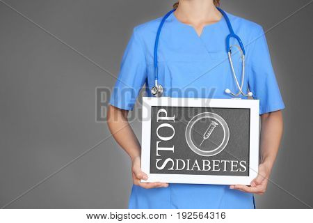 Health care concept. Doctor holding small chalkboard with text STOP DIABETES on gray background