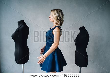Woman fashion designer in a blue dress is standing near the mannequins. Lips with injection