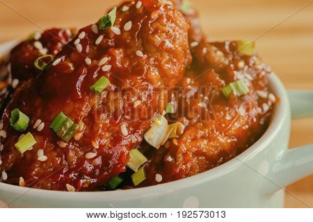 Korean fried chicken wings sprinkled with sesame and spring-onion on wood plate. Korean barbecue chicken wing delicious,moist and spicy. Close up on fried chicken wings in Korean style on wood table. Chicken barbecue. Chicken wings.