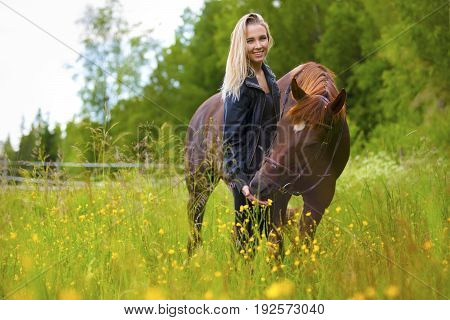 Smiling and beautiful young woman feeding her adult arabian horse standing in a field. Relationship between human and animal.