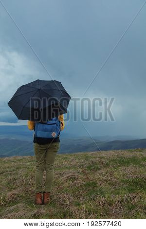Girl with umbrella watching rain-storm in the distanant landscape.