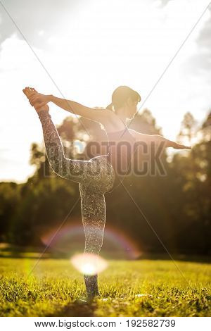 Caucasian woman in yoga standing balance Natarajasana, known as dancer pose, on meadow in early morning. Back view