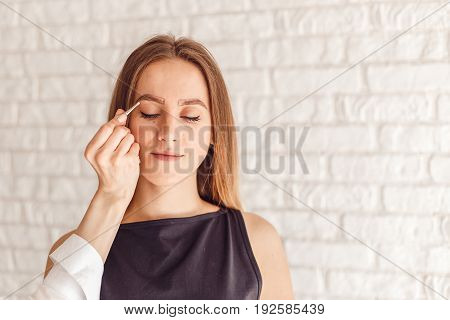 Portrait of a model and the masters hand with tweezers. Young woman tweezing her eyebrows.