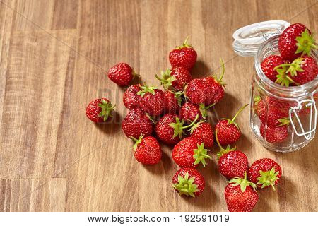 Fresh red strawberries for jam in a glass jar on the brown wooden table. Many strawberries in the glass jar and on the table. Horizontal photo. Seasonal fruits. Food backgrounds and still-life. Concept of the vitamin food.