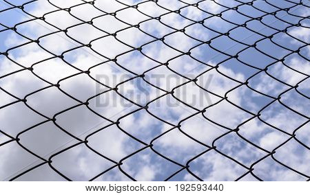 Metallic fence against the blue sky with clouds.Net metallic pattern barrier against blue sky. Chain Link Fence against  Cloudy Blue Sky.