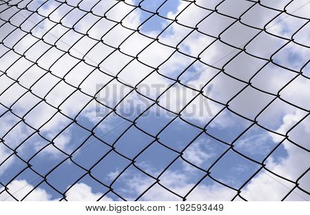 Metallic fence against the blue sky with clouds.Net metallic pattern barrier against blue sky. Chain Link Fence against  Cloudy Blue Sky.