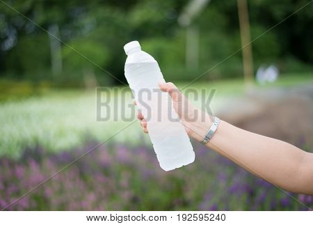 Woman hand holding bottle of water on nature background.