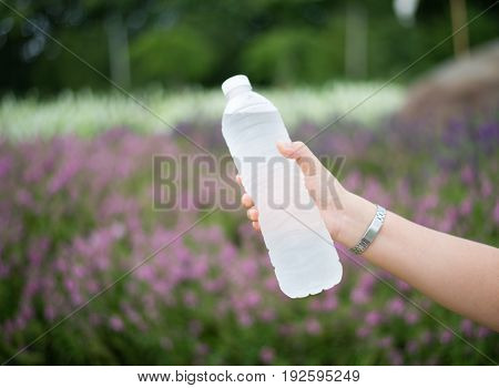 Woman hand holding bottle of water on nature background.