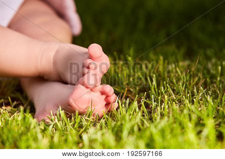 Close up of baby's feet on the green grass on the meadow at warm day. Horizontal croped photo. Small cute feet of liitle child. Concept of the happy babies.