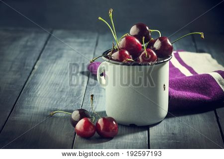 Ripe cherries in an iron mug on a dark blue wooden background. With copy space.