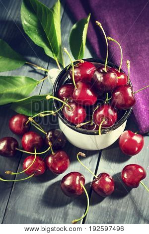 Ripe cherries in an iron mug on a dark blue wooden background. With copy space.