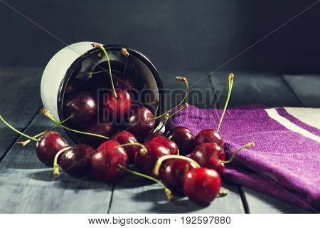 Ripe cherries in an iron mug on a dark blue wooden background. With copy space.