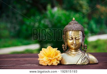 Golden antique Buddha statue on a blurred green background. Buddha and flowers. Concept religion. Copy space