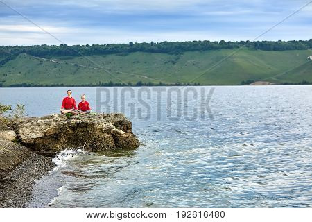 Sporty mother and daughter doing yoga on the rock near beautiful river. Beautiful mother and daughter dressed in the sportwear and barefoot. Horizontal photo with beauty landscape. Concept of the healthy and active lifestyle.