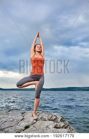 Young sporty woman doing different variants of yoga position on a rocky rivershore. Beauty woman dressed in the sportwear and barefoot. Beautiful landscape like a background. Concept of the healthy and active lifestyle.