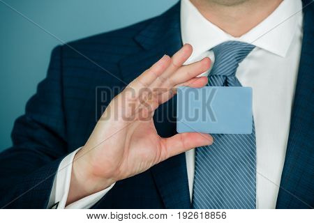 hand holding blank bank or business card in formal suit with stylish tie on blue background. Economy credit ecash banking ethics and information
