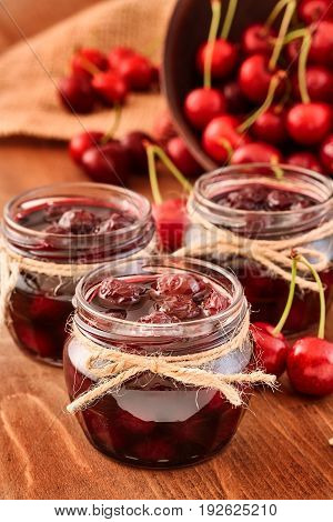 Cherry jam on wooden background in glass jars