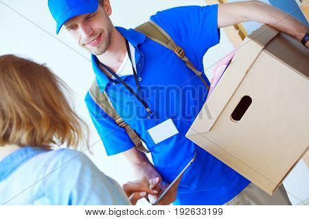 Smiling delivery man in blue uniform delivering parcel box to recipient - courier service concept