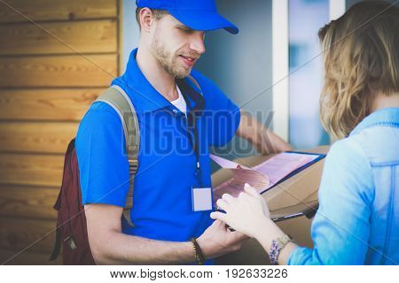 Smiling delivery man in blue uniform delivering parcel box to recipient - courier service concept
