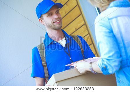 Smiling delivery man in blue uniform delivering parcel box to recipient - courier service concept