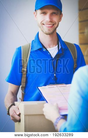 Smiling delivery man in blue uniform delivering parcel box to recipient - courier service concept