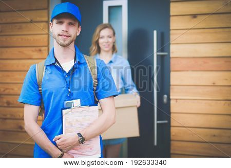 Smiling delivery man in blue uniform delivering parcel box to recipient - courier service concept