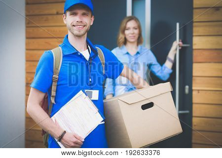 Smiling delivery man in blue uniform delivering parcel box to recipient - courier service concept