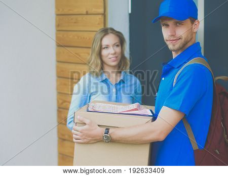 Smiling delivery man in blue uniform delivering parcel box to recipient - courier service concept