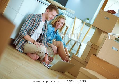 Young couple moving in new home.Sitting on floor and relaxing after unpacking.Looking something on laptop