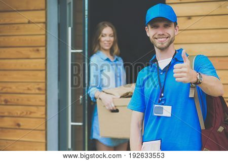 Smiling delivery man in blue uniform delivering parcel box to recipient - courier service concept