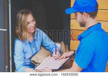 Smiling delivery man in blue uniform delivering parcel box to recipient - courier service concept