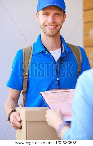 Smiling delivery man in blue uniform delivering parcel box to recipient - courier service concept