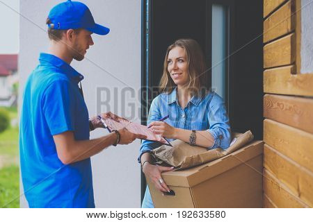Smiling delivery man in blue uniform delivering parcel box to recipient - courier service concept