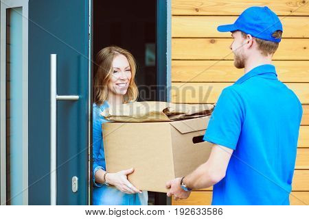 Smiling delivery man in blue uniform delivering parcel box to recipient - courier service concept