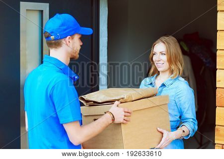 Smiling delivery man in blue uniform delivering parcel box to recipient - courier service concept