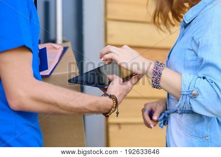 Smiling delivery man in blue uniform delivering parcel box to recipient - courier service concept