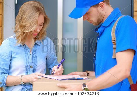 Smiling delivery man in blue uniform delivering parcel box to recipient - courier service concept