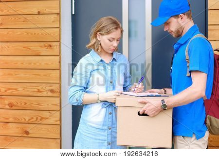 Smiling delivery man in blue uniform delivering parcel box to recipient - courier service concept