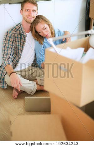 Young couple moving in new home.Sitting on floor and relaxing after unpacking.Looking something on laptop