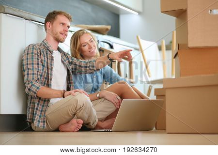Young couple moving in new home.Sitting on floor and relaxing after unpacking.Looking something on laptop