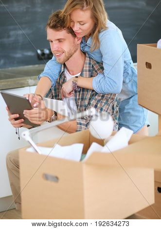 Young couple moving in new home.Sitting and relaxing after unpacking.Looking something on laptop