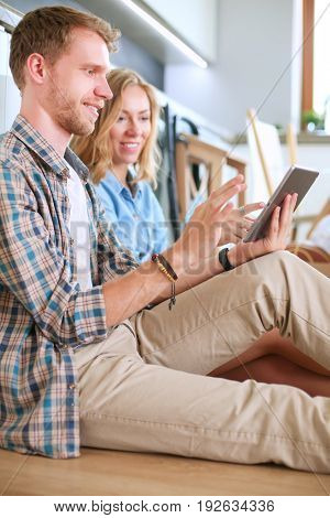 Young couple moving in new home.Sitting on floor and relaxing after unpacking.Looking something on laptop