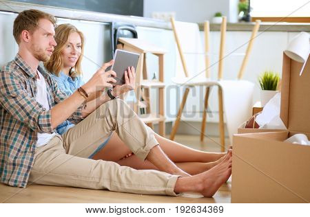 Young couple moving in new home.Sitting on floor and relaxing after unpacking.Looking something on laptop