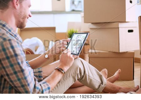 Young couple moving in new home.Sitting on floor and relaxing after unpacking.Looking something on laptop