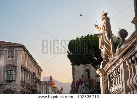 Statue outside the Church of St. Agatha in Catania Sicily with the town and Mount Etna in the background